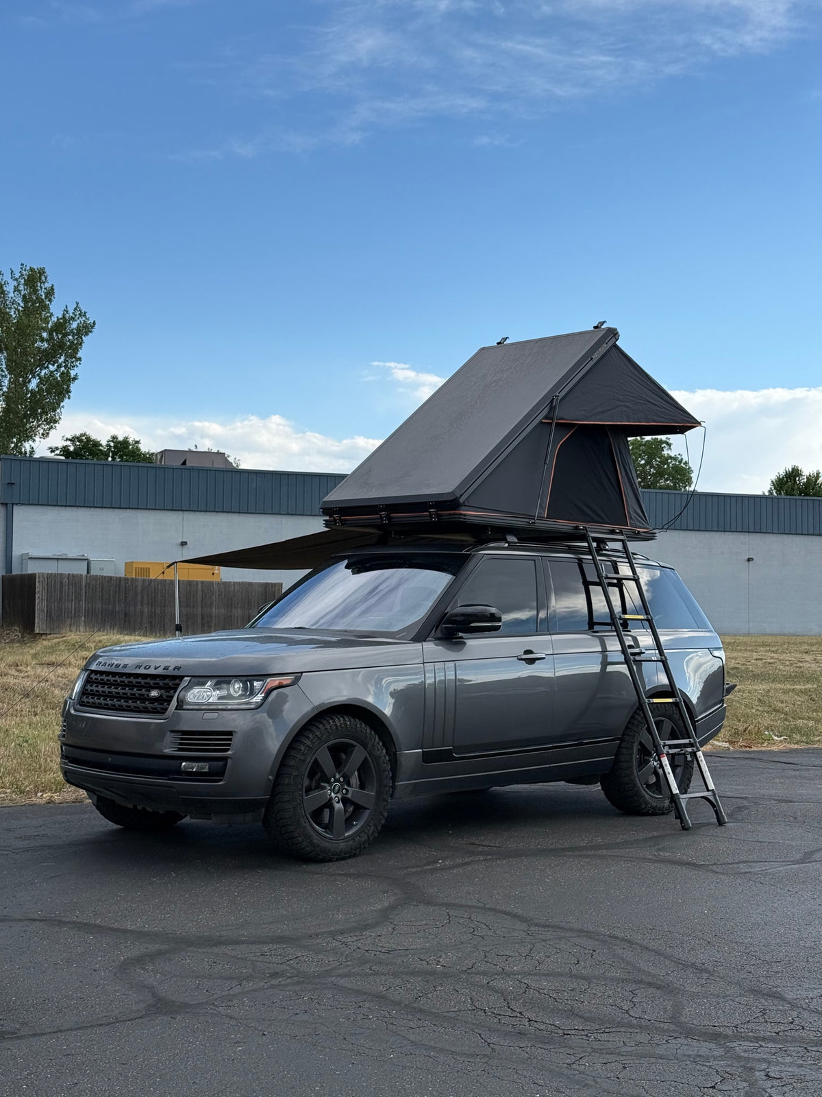 Experience adventure with this grey Range Rover RV rental, featuring a rooftop tent, awning, and off-road tires.