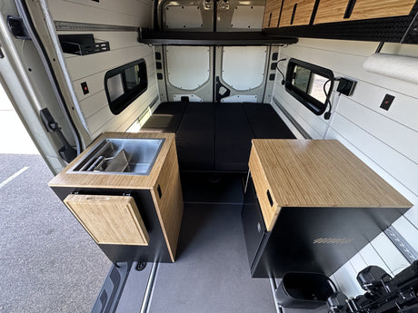 Inside an RV rental camper van: efficient layout with a left-side kitchen sink, right-side storage, and rear bed.