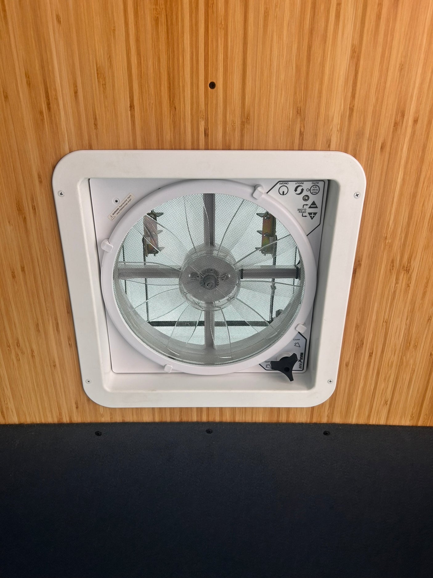 A white Maxxfan ceiling vent installed in an RV rental, set against warm bamboo paneling.