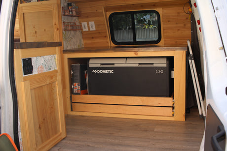 Inside an RV rental: a custom wood interior with a Dometic fridge, power outlets, and a cozy built-in setup.