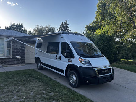 White Ram ProMaster camper van with extended awning parked on a driveway. Ideal for your next rv rental adventure.