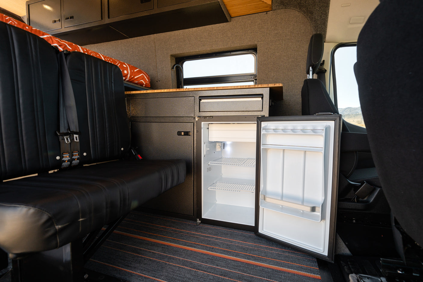 Inside this RV rental: a modern camper van with a comfy bench seat, custom kitchenette, and an open refrigerator.