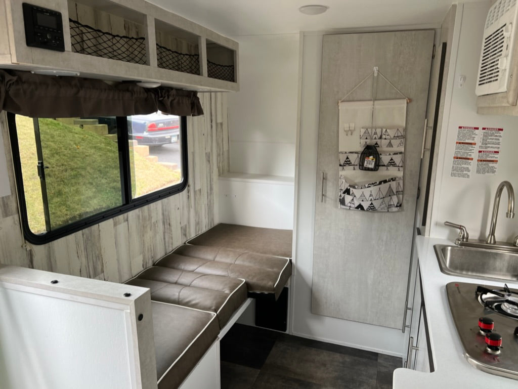Inside a modern RV rental: light wood-look interior walls, kitchen, cushioned seating/bed, and net storage.
