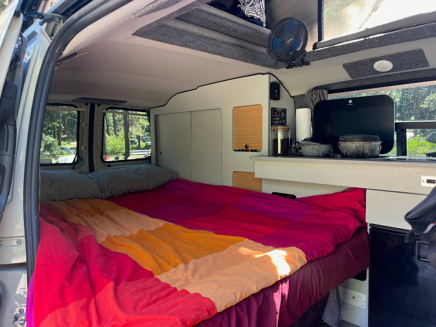 Cozy camper van interior with colorful bed & built-in kitchen. Ideal for an RV rental getaway.