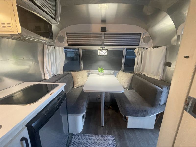 Modern rv rental interior: kitchenette with microwave, and cozy dinette with grey cushions, white table, and decorative lighting. — photo 6