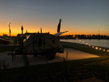 Enjoy a beautiful sunset at a waterfront RV rental campsite, featuring a 'Freesolo' teardrop trailer and string lights.
