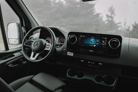 Inside a modern Mercedes-Benz Sprinter RV rental, featuring its advanced cockpit, dashboard, and infotainment system on a rainy day.