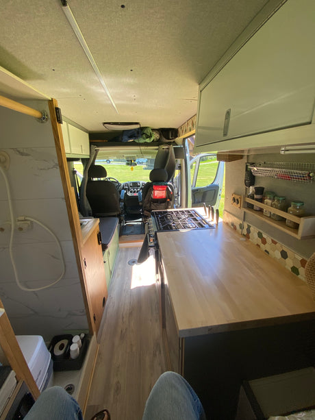 Bright rv rental interior: view of a functional camper van kitchen with a stove, shower, and front cabin. Perfect for adventures.