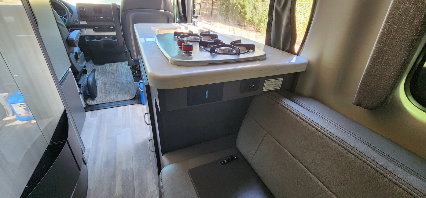 Explore the modern kitchen and living area of this comfortable RV rental, featuring a stovetop, sink, and versatile seating.