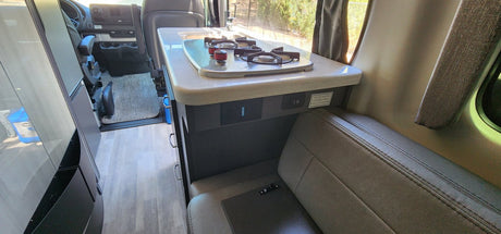 Explore the modern kitchen and living area of this comfortable RV rental, featuring a stovetop, sink, and versatile seating.
