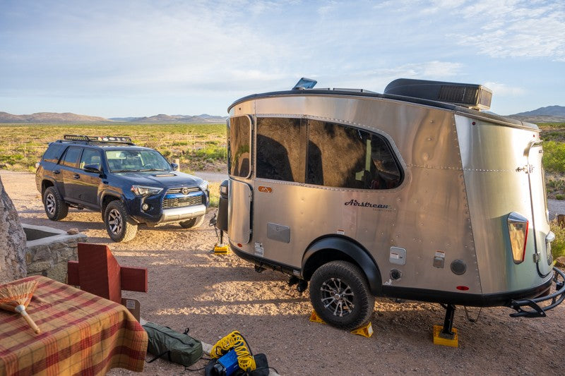An Airstream Basecamp RV rental hitched to a dark blue SUV, parked at a sunny desert campsite. — photo 8