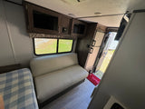 Interior of an rv rental features a cozy bed, sofa, overhead cabinets, and a kitchen area, providing a comfortable camper living space.