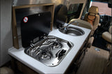 Compact kitchenette in this RV rental, featuring a two-burner stove and sink. Perfect for mobile living and travel.
