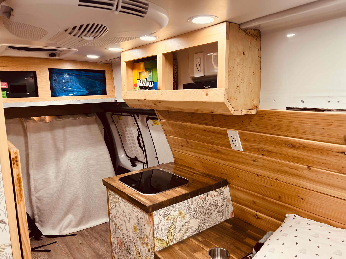 Bright rv rental interior, showing wooden walls, integrated sink/cooktop, overhead storage, and a sleeping area.