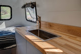 Inside an RV rental: a compact kitchen with a light wood countertop, stainless steel sink, and modern faucet, beside a bed.