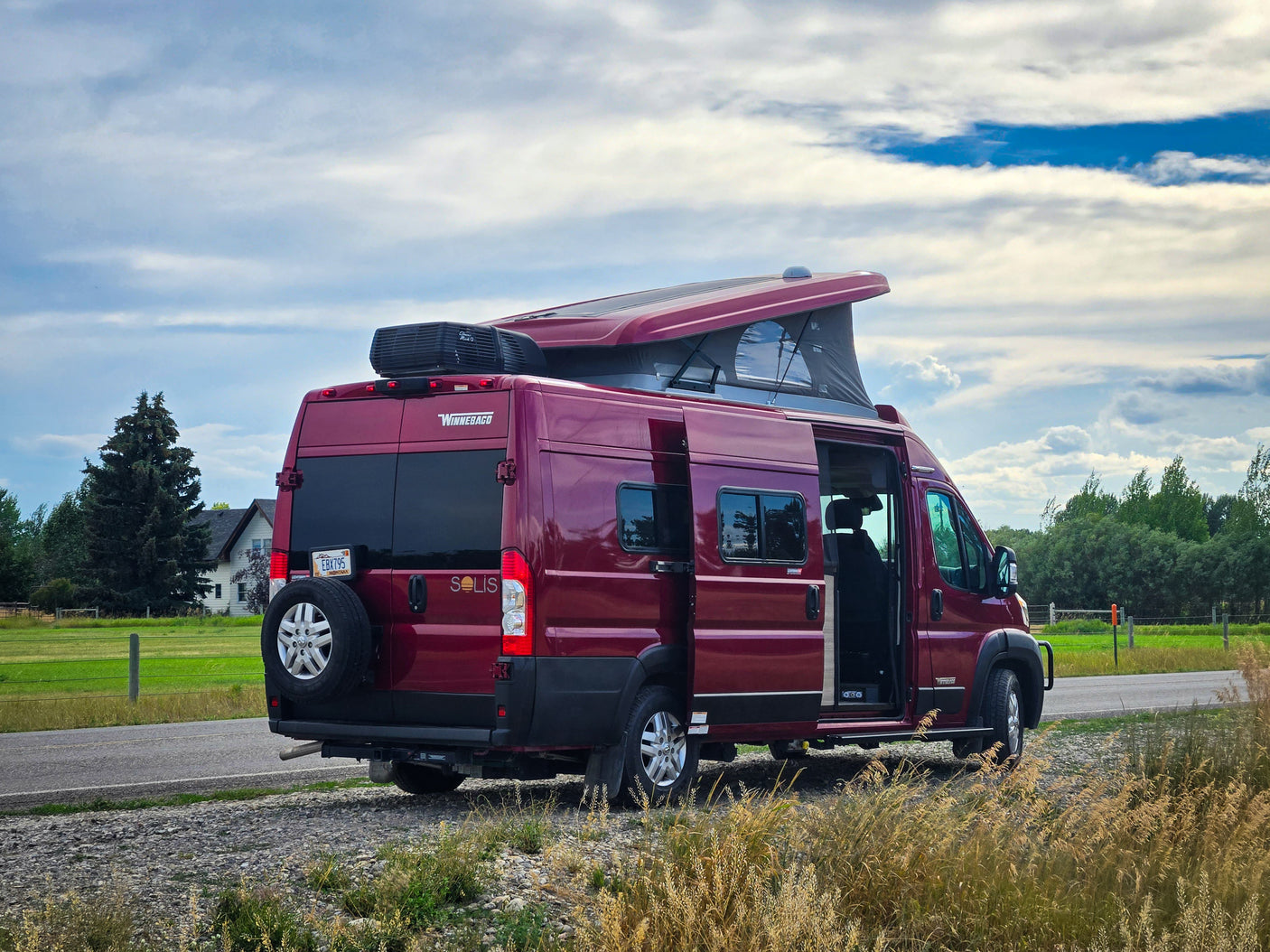 Maroon Winnebago Solis camper van (RV rental) parked on a roadside with its pop-top extended.