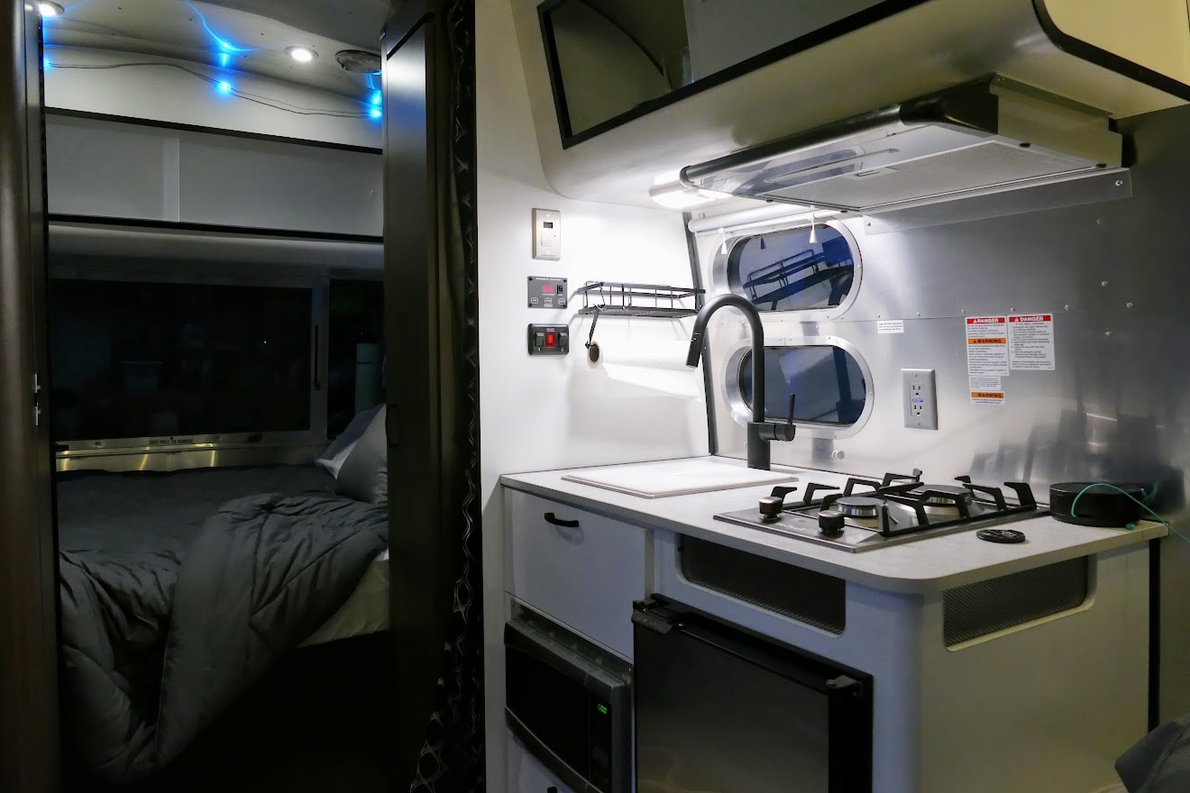 Modern RV rental features a well-equipped kitchen with sink, stove, microwave, and a private, cozy bedroom with blue lights. — photo 9