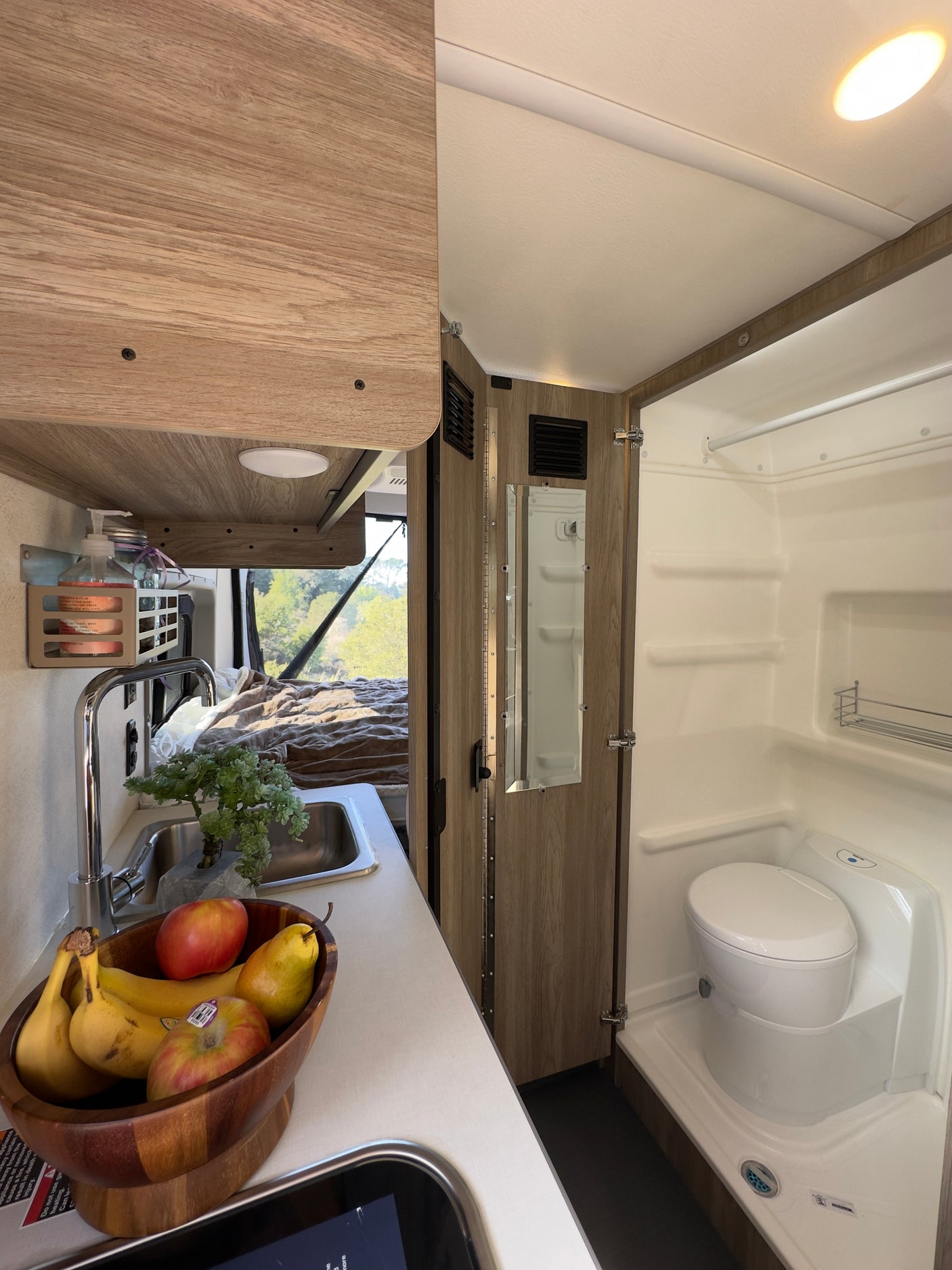 RV rental interior: A compact kitchen with sink and fresh fruit, plus a wet bath with toilet and shower, ready for van life adventures.