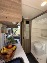 RV rental interior: A compact kitchen with sink and fresh fruit, plus a wet bath with toilet and shower, ready for van life adventures.