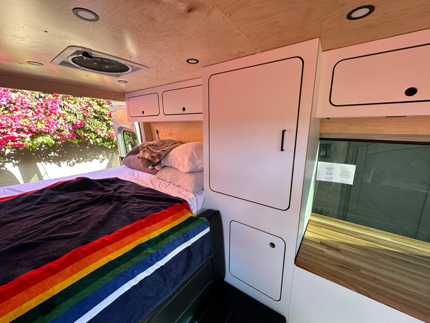Cozy camper van interior for your next RV rental, featuring a bed, storage, and natural light from a window overlooking flowers. — photo 10