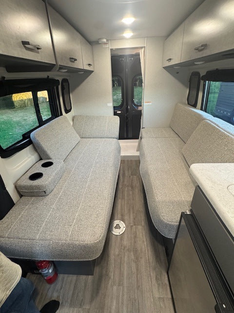 Spacious RV rental interior featuring light grey bench seating, overhead cabinets, and wood-look flooring. Perfect for travel comfort.