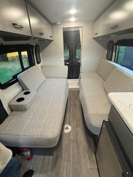 Spacious RV rental interior featuring light grey bench seating, overhead cabinets, and wood-look flooring. Perfect for travel comfort.