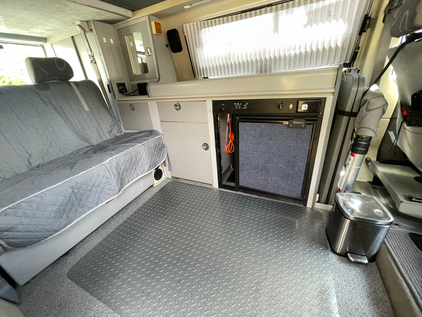 Inside this RV rental: bench seat, built-in fridge, cabinets, and durable diamond plate flooring for travel comfort.