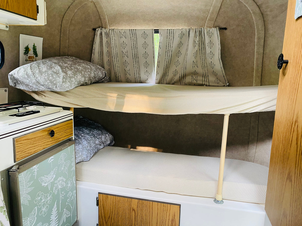 Compact RV rental interior featuring cozy bunk beds, a Dometic fridge, and window curtains. — photo 9
