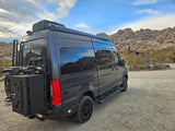 Rugged dark grey 4x4 camper van, ideal as an rv rental, ready for desert adventures amidst rocky landscapes.