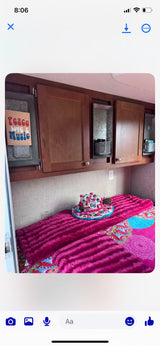 Inside a colorful **RV rental**: bright pink bed with Route 66 hat, wood cabinets, and a 'Peace Love & Music' sign.