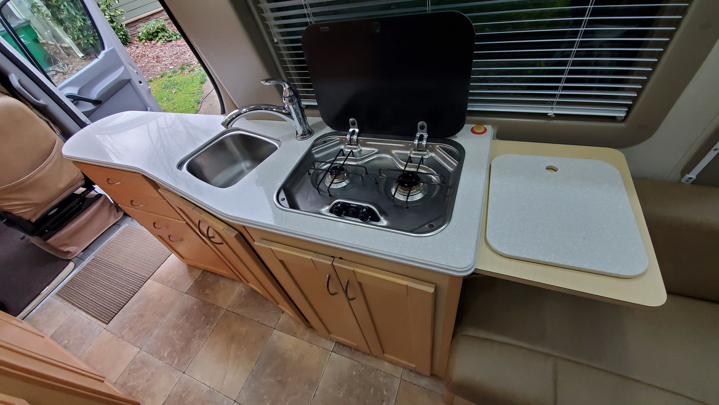 Inside an RV rental, discover a compact kitchen featuring a sink, two-burner stove, and expandable counter space.