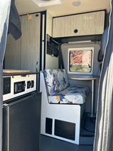Cozy rv rental interior: floral dinette, window with desert view, kitchen counter with controls, and overhead storage.