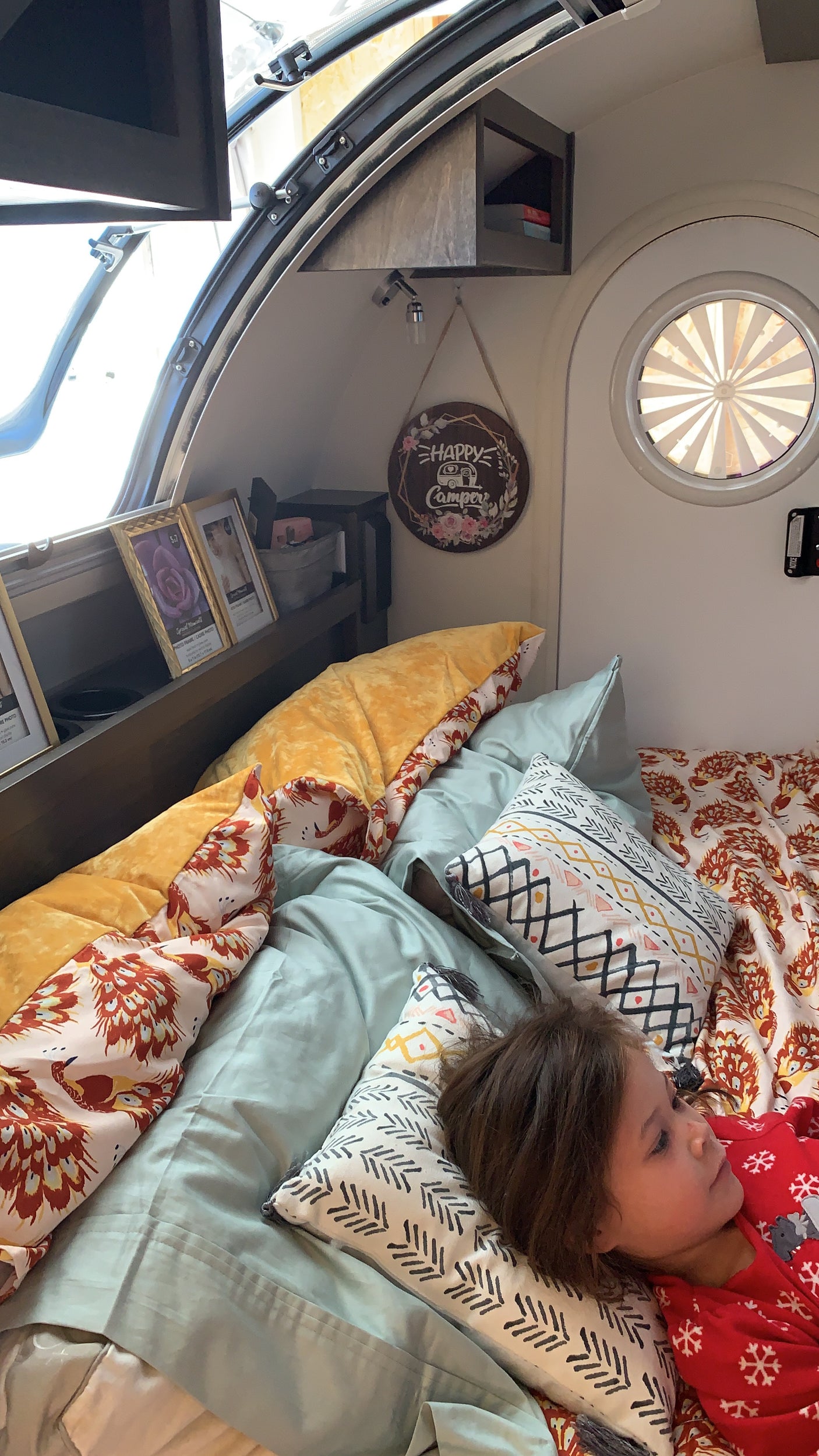 Cozy RV rental interior with a child resting on a colorful bed, framed photos, and camper decor.