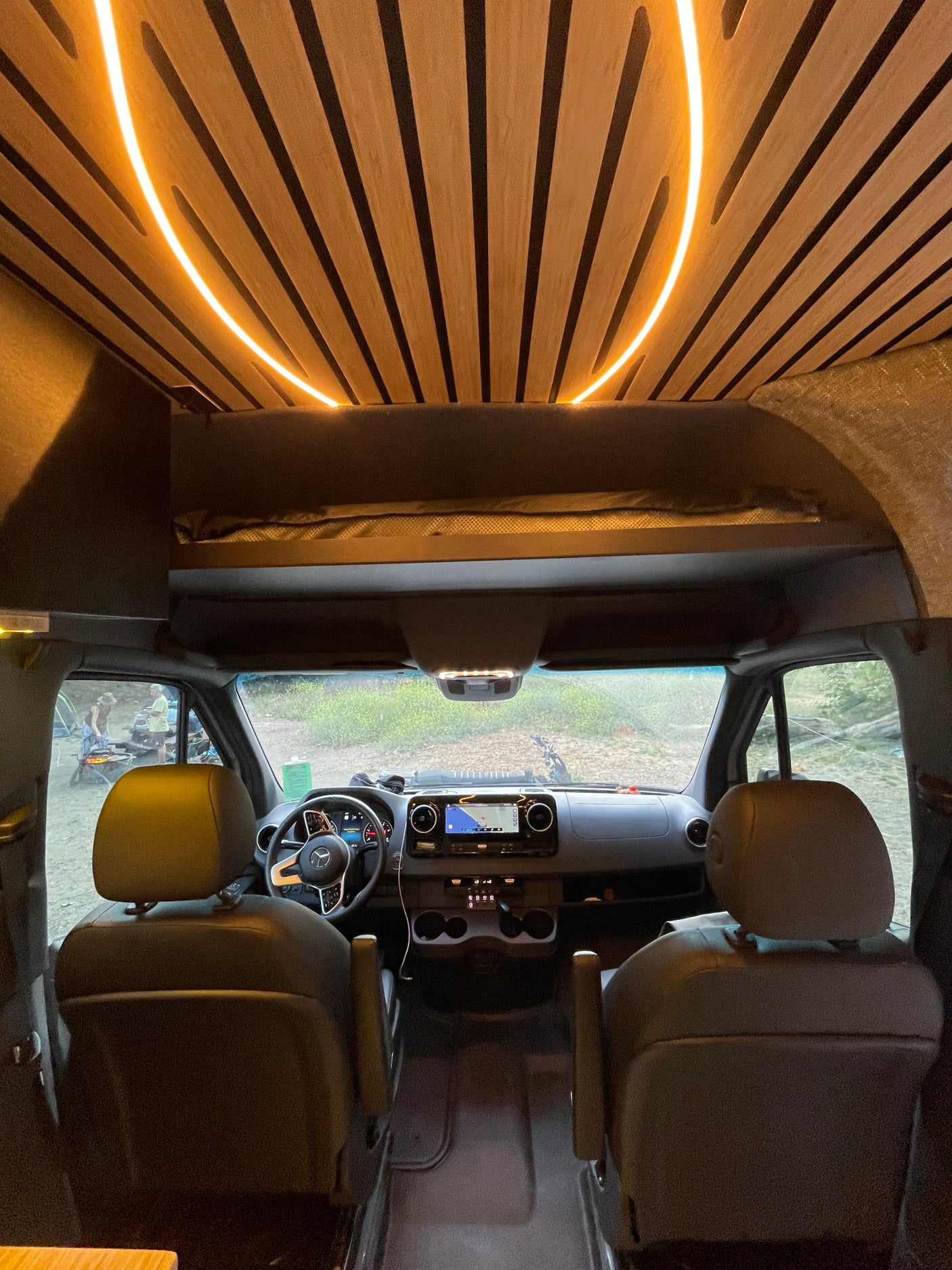 Experience comfort in this RV rental: unique wooden ceiling with curved LED lighting, modern front cabin, and a view of the outdoors.