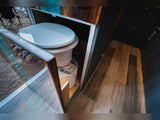 An open panel reveals a discreet composting toilet inside an RV rental, showing a compact, practical mobile bathroom solution.