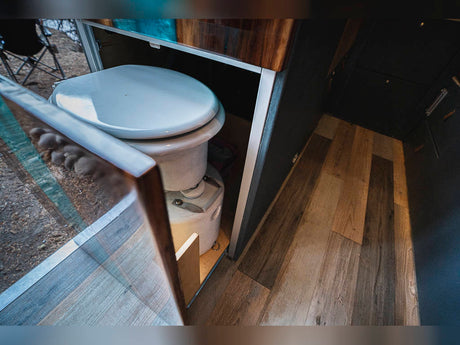 An open panel reveals a discreet composting toilet inside an RV rental, showing a compact, practical mobile bathroom solution.