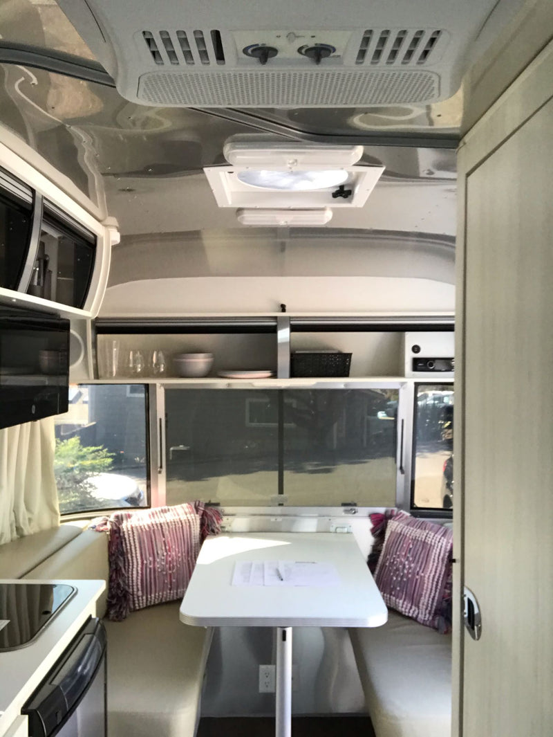  and large windows revealing parked vehicles outside.|Cozy Airstream RV rental bedroom with gray bedding — photo 6