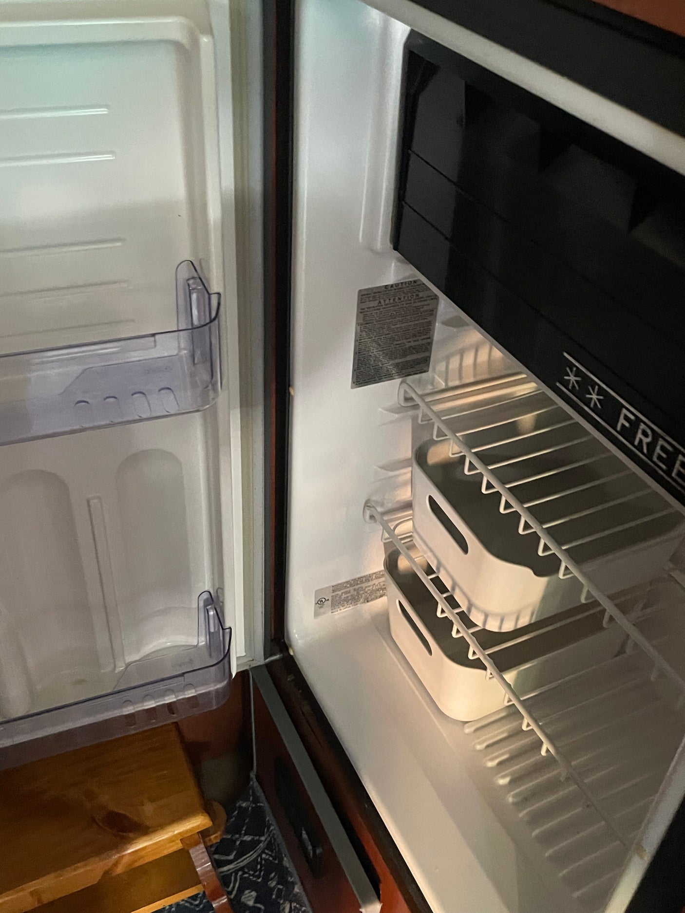 Open, empty compact RV rental refrigerator, revealing its interior with a freezer, wire shelves, and two storage bins.