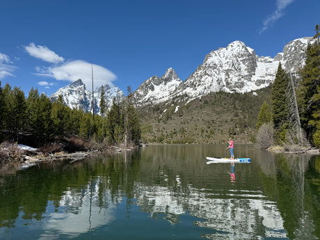 Paddleboarder on a clear mountain lake, snowy peaks reflecting. Ideal RV rental destination!
