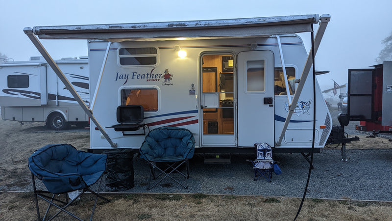 This RV rental, a Jay Feather travel trailer, is set up for camping with an awning, chairs, and grill, providing cozy outdoor living. — photo 14