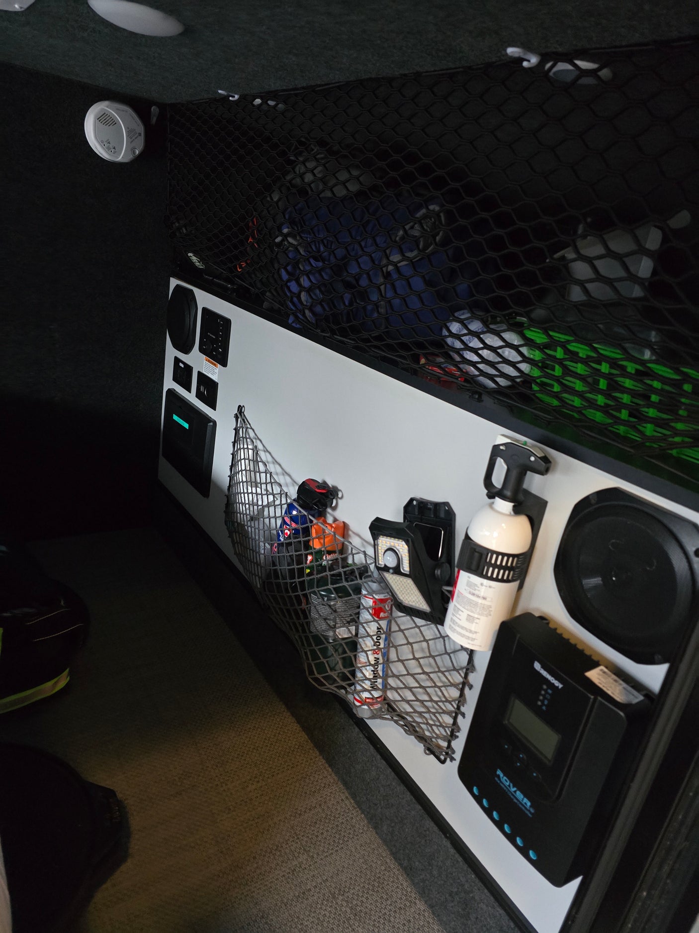 Explore a modern RV rental interior with organized cargo nets, control panel, Renogy solar charge controller, fire extinguisher, and detector.