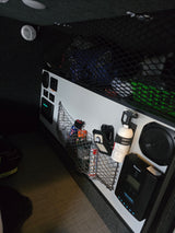 Explore a modern RV rental interior with organized cargo nets, control panel, Renogy solar charge controller, fire extinguisher, and detector.