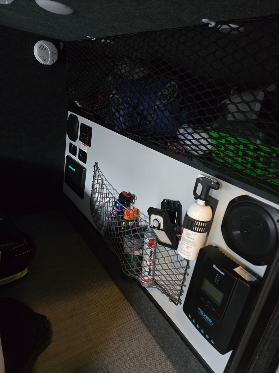 Explore a modern RV rental interior with organized cargo nets, control panel, Renogy solar charge controller, fire extinguisher, and detector.