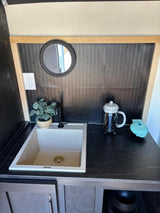 RV rental: Compact kitchenette with light sink, dark counter, black backsplash, plant, French press, waffle maker.