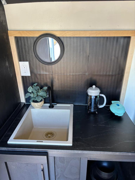 RV rental: Compact kitchenette with light sink, dark counter, black backsplash, plant, French press, waffle maker.
