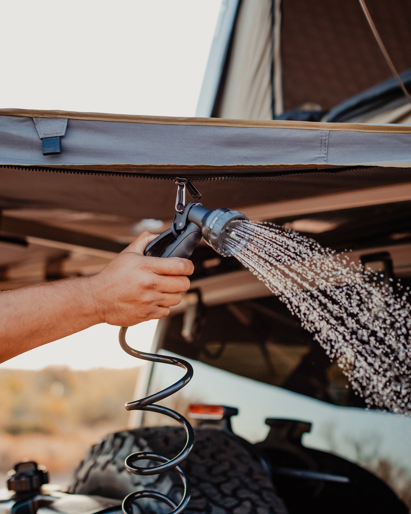An RV rental setup shows a person using a portable shower head, spraying water, ideal for outdoor camping adventures.