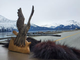 An RV rental journey: a carved bird statue on the dashboard faces a road, serene lake, and majestic snow-capped mountains.