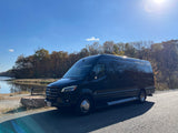Black Mercedes-Benz Sprinter luxury van, an ideal rv rental, parked by a lake with autumn foliage.
