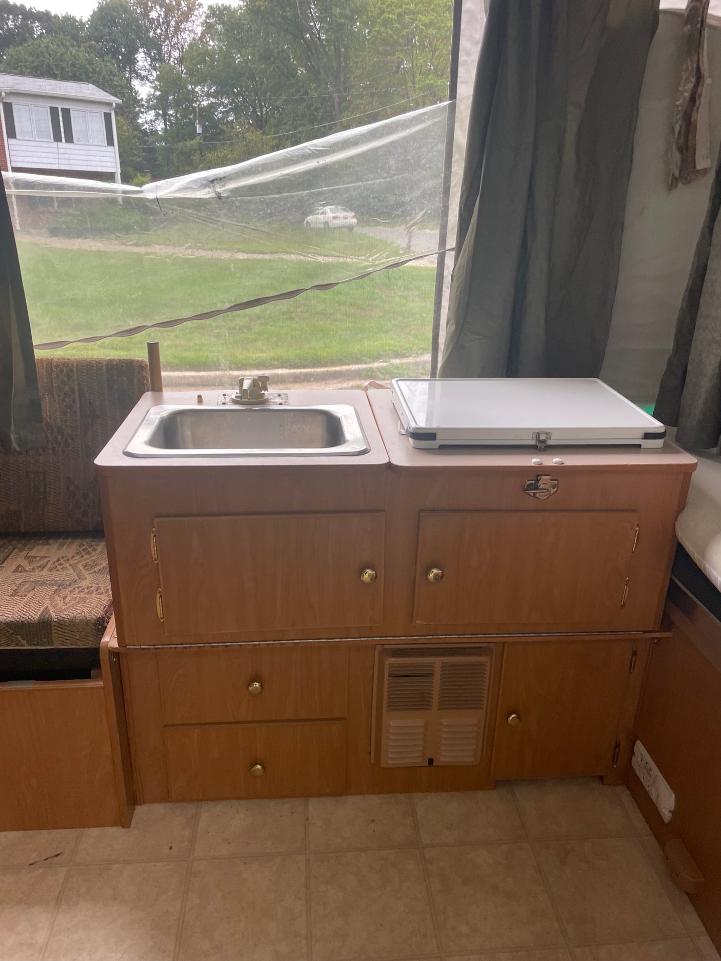 RV rental pop-up camper interior, showing a compact kitchen with a sink, light wood cabinets, and a heater vent.