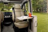 RV rental interior: driver's beige seat with dash, plus a side table holding a drink & notebook. Scenic outdoor view.